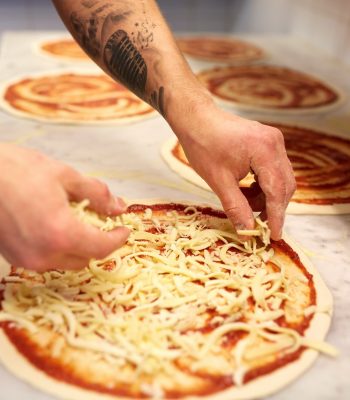 cook adding grated cheese to pizza at pizzeria